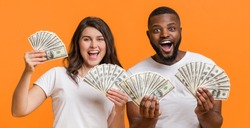 Money prize. Joyful mixed-race couple holding a lot of dollar cash and looking at camera, posing over orange background
