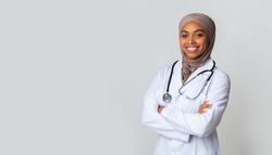Medical Care For Muslim Women. Portrait Of Smiling Black Female Doctor In Hijab And White Coat Posing With Folded Arms Over Light Background, Panorama