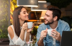 Dating. Young couple tasting coffee drinks enjoying flirt and conversation during weekend date sitting in cozy cafe