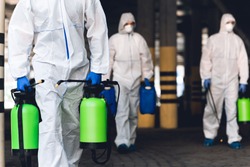 Warning, coronavirus disinfection. Men in virus protective suits carrying spray bottles with chemicals, blurred background
