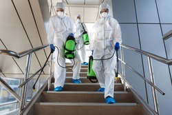 People wearing protective suits disinfecting stairs with spray chemicals to prevent the spreading of the coronavirus