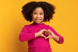 Love Concept. Adorable Little African American Girl Showing Heart Gesture With Hands Over Yellow Background In Studio, Free Space