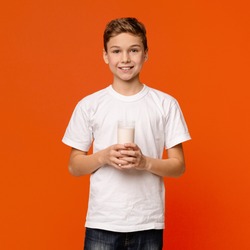 Milk lover. Cheerful teenage boy smiling with glass of fresh milk, orange background