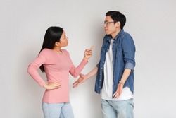 You are lying. Asian angry girl scolding her surprised boyfriend, grey studio background