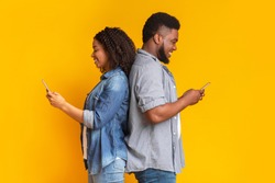 Social Network Addiction. Black Millennial Couple Using Smartphones, Standing Back To Back And Ignoring Each Other, Yellow Background