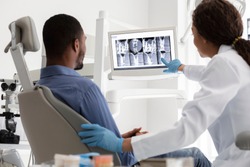 African female dentist and male patient watching xray on digital screen at modern clinic