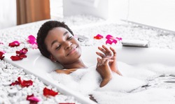 Smiling and relaxing african american woman with closed eyes takes bath with foam and petals