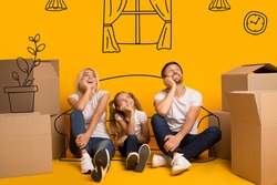 Happy parents and their kid with carton boxes imagining their new home on orange background with drawings