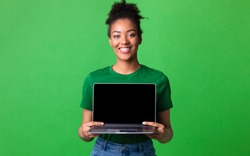 Useful Website. Cheerful afro girl holding laptop computer, showing blank screen over green studio wall, mock up