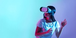 High technology for games. Girl in virtual glasses turns around and looks at something, in light of neon, panorama, copy space