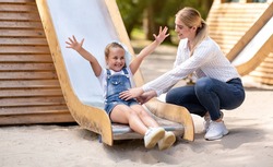 Little Girl Riding A Slide Having Fun On Playground Spending Weekend With Mother In Park. Happy Childhood Concept