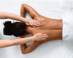 Slim black woman receiving full body massage at modern spa, top view