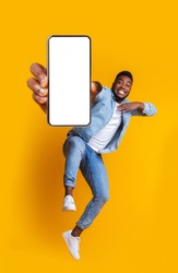 Advertisement for mobile application. Excited african guy dancing over yellow background, showing modern smartphone with empty screen, collage