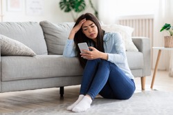Smartphone Addiction And Depression. Upset Asian Girl Sitting On Floor At Home With Smartphone, Looking Sadly To Device Screen