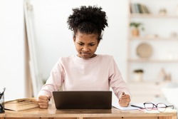 Angry Black Teen Girl At Laptop Looking At Screen Clenching Fists Sitting At Desk At Home. Computer Problem Concept