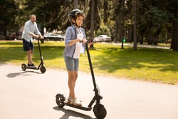 Youth Leisure Concept. Full length portrait of excited boy riding black e-scooter with his dad in background, free space