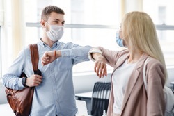 Say hello and greet, social distance and return to work after quarantine. Millennial man and woman in protective masks are touched by elbows in interior of office during COVID-19 epidemic, free space
