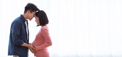 Pregnancy Happiness. Happy Japanese Husband Hugging And Touching Pregnant Wife's Belly Standing Near Window Indoors. Loving Asian Couple Awaiting Baby, Cute Parents-To-Be. Panorama, Copy Space