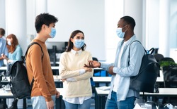 Healthcare, Education, Lifestyle And People Concept. Group of smiling diverse international students wearing protective medical masks and talking, standing in lecture hall at the university