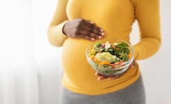 Closeup of bowl with fresh salad in pregnant black lady hands, copy space. Expecting african american woman eating vegetables during pregnancy, nutrition during carrying child concept