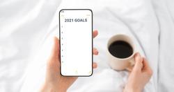 2021 New Year Goals Checklist. Hands Holding Smartphone With Future Goal And Plans List For Upcoming New Year Making Yearly Planning For 2021 Lying In Bed Indoor. Panorama, Selective Focus, Cropped