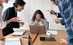 Workplace Conflict And Bullying. Aggressive Coworkers Yelling At Victimized Businesswoman Sitting At Desk In Modern Office. Corporate Communication Problem, Quarrels And Bad Attitude At Work