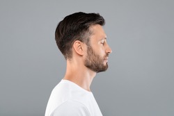Side view of middle-aged bearded man in white t-shirt over grey studio background, copy space. Profile portrait of handsome man with closed eyes posing on gray, standing straight and looking aside