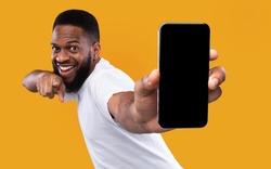 Mobile App Advertisement. Excited Black Man Showing Smartphone Empty Screen Recommending App Posing Over Yellow Studio Background, Smiling To Camera. Check This Out, Cellphone Display Mockup