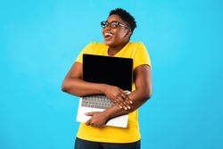 Happy Overweight Black Woman Hugging Laptop Computer With Blank Screen Posing Standing Over Blue Studio Background. Online Technology. Website Advertisement Concept. Mockup