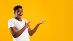 Excited Plus-Size Black Woman Showing Invisible Object Pointing Fingers Aside Advertising Your Text Posing Standing On Yellow Studio Background, Smiling To Camera. Blank Space, Panorama