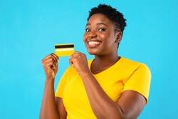 Oversized African Woman Holding Yellow Credit Card Showing It To Camera Advertising Bank Posing Over Blue Studio Background. Banking, Money And Finance, Financial Advertisement Concept