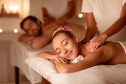 Couple Relaxing Receiving Back Massage Lying Closing Eyes At Romantic Luxury Spa With Burning Candles And Flowers. Wellness And Body Relaxation Therapy. Selective Focus, Low Light