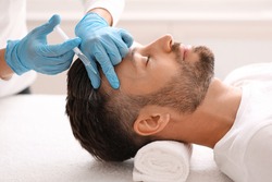 Side view of handsome middle aged man getting hair treatment at beauty salon. Man having mesotherapy session at aesthetic clinic, therapist hands in gloves making injection in scalp, closeup
