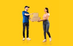 Parcel Delivery. Woman Receiving Boxes From Male Courier Standing Over Yellow Studio Background. Post Package Delivering And Transportation, Couriers Service Concept. Full Length