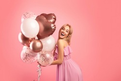 Carefree young lady with holiday balloons partying, celebrating birthday or anniversary over pink studio background. Beautiful female model having special festive occassion, enjoying her birthday
