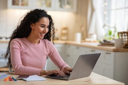 Remote Work. Beautiful Young Freelancer Lady Working With Laptop In Kitchen, Happy Millennial Woman Using Computer At Home, Sitting At Table In Cozy Interior, Enjoying Online Job, Free Space