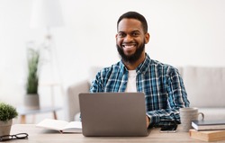 Cheerful Black Businessman Sitting At Laptop Smiling To Camera Working Online On Computer In Modern Office. Entrepreneurship And Own Business. Successful Career Concept. Selective Focus