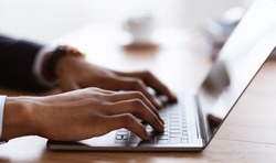 Selective focus on male hands typing on laptop keyboard, cropped, side view. African american businessman sending emails to clients or assistant. Modern technologies and business concept