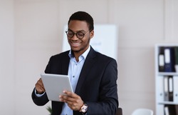 Positive black guy young entrepreneur using digital tablet in office, copy space. Smiling african american manager checking his agenda on pad, enjoying modern technologies for business