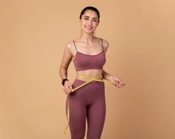 Weight Loss And Healthy Lifestyle Concept. Smiling slim woman measuring her waist with yellow tape over pastel studio background. Fit young lady in perfect shape, happy with her body