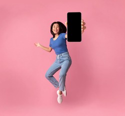 Happy asian young woman showing empty smartphone screen while jumping up over pink studio background, collage, full size photo. Excited lady recommending nice and useful mobile application