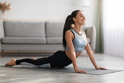Active young woman in sportswear practicing yoga at home, laying on fitness mat in living room and stretching her body, copy space. Downward-facing dog yoga pose, yoga practice at home concept