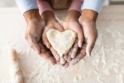 Love And Care Concept. Closeup above top view of unrecognizable african american man and girl baking cake in the kitchen and holding dough in heart shape in hands, dad and daughter cooking together