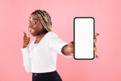 Trendy Mobile Phone. Excited young black lady holding smartphone with white empty screen in hand, showing device close to camera. Gadget with blank space, mockup, selective focus, blurred background