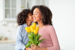 I Love You, Mommy. Portrait of cute African American girl kissing her mum in cheek and giving bunch of yellow tulips flowers, greeting woman with holiday, Women's or Mother's Day or birthday.