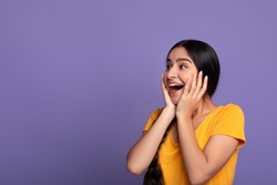 Huge Sale Or Promo Concept. Amazed indian woman screaming and touching her face in disbelief, looking at free copy space on purple studio background. Astonished young lady with open mouth