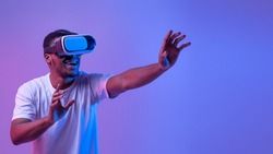 Virtual Experience. Excited African American Man In neon Lighting Wearing VR Headset, Touching Air While Playing Video Game, Amazed Black Guy Standing Over Purple Background, Panorama With Copy Space