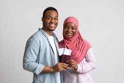 Going vacation. Smiling young muslim couple holding flying tickets and passports, got visa, happy guy and his girlfriend travellers getting ready for trip over grey studio background, copy space
