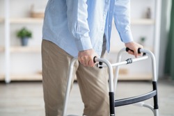 Cropped view of elderly man walking with frame at home, closeup. Unrecognizable senior male using medical equipment to move around his house. Disabled older person in need of professional help