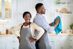 Portrait of positive black woman and her husband wiping dishes at kitchen